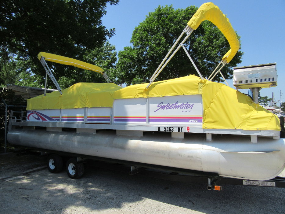 A white pontoon parked in a lot below trees with a yellow boat canopy on top at Cope Marine of it.