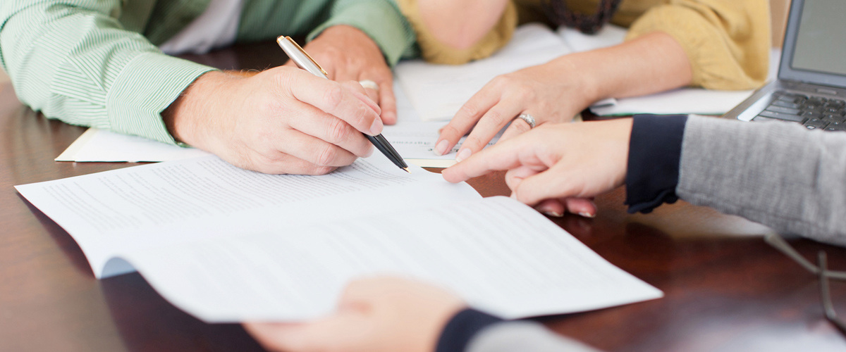 Two individuals pointing to a pen that a third individual is using to write on paper.